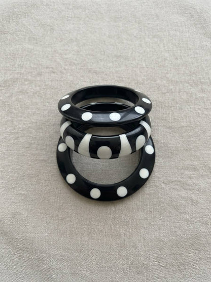 Set of three black resin bangles with white polka dots and stripe pattern stacked upright on a grey linen background
