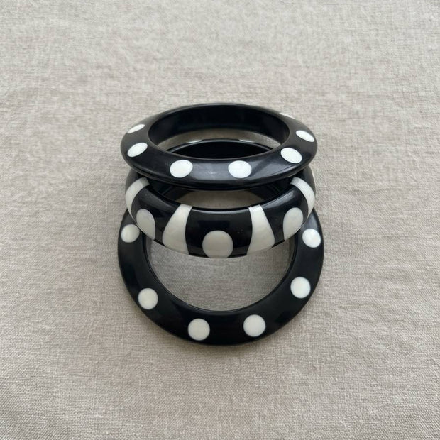 Set of three black resin bangles with white polka dots and stripe pattern stacked upright on a grey linen background