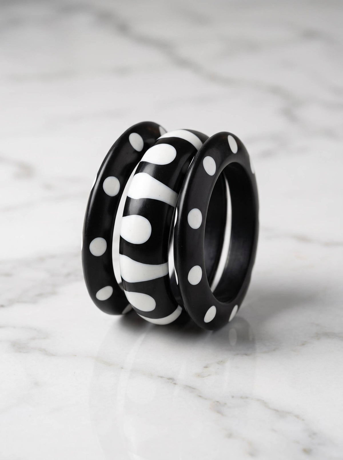 Three black resin bangles with white polka dot and zebra stripe designs grouped together on a white marble surface