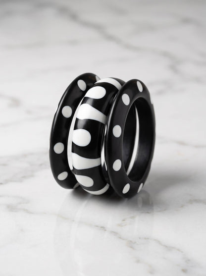 Three black resin bangles with white polka dot and zebra stripe designs grouped together on a white marble surface