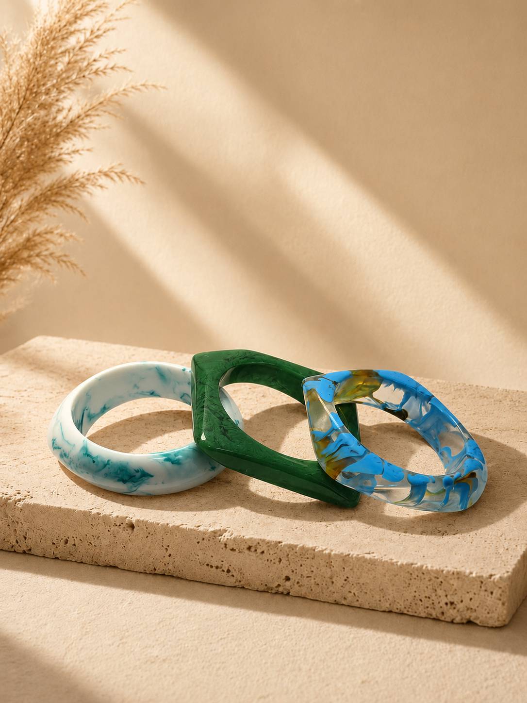 Three resin marble bangles stacked on a sandy stone surface with pampas grass in the background