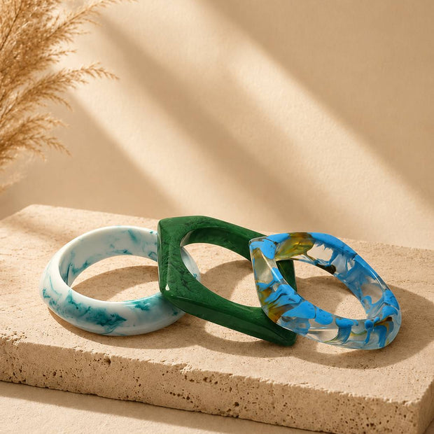Three resin marble bangles stacked on a sandy stone surface with pampas grass in the background