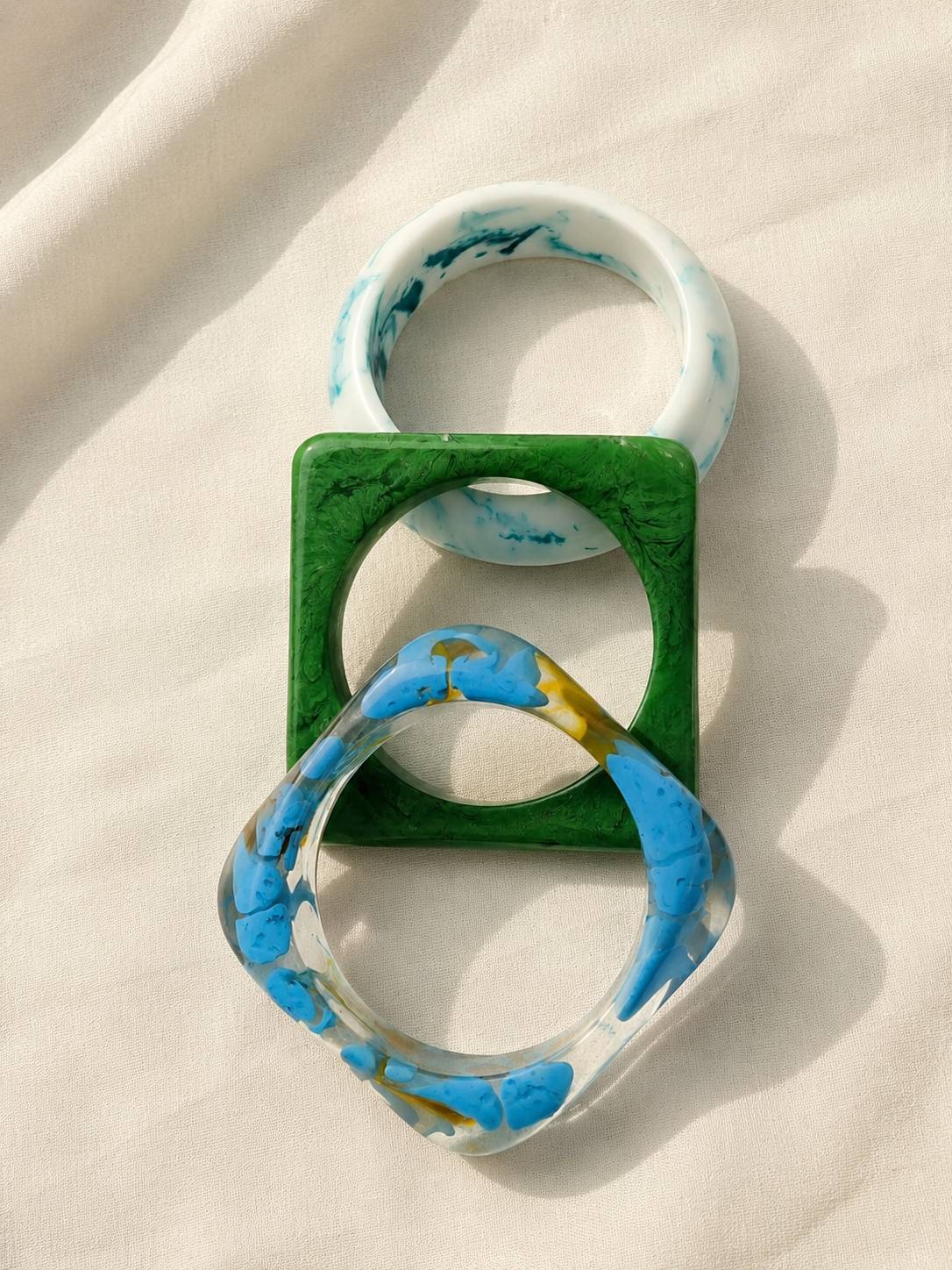 Top-down view of three interlocked resin bangles on white fabric showing round and square shapes