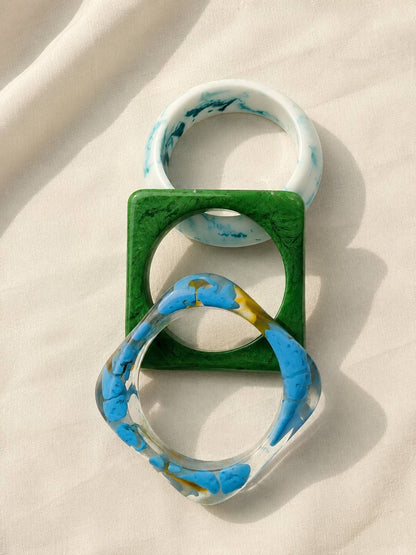 Top-down view of three interlocked resin bangles on white fabric showing round and square shapes