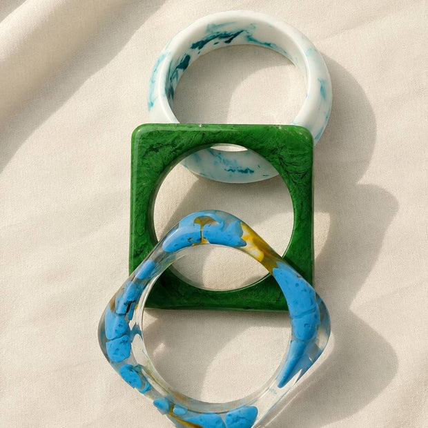 Top-down view of three interlocked resin bangles on white fabric showing round and square shapes