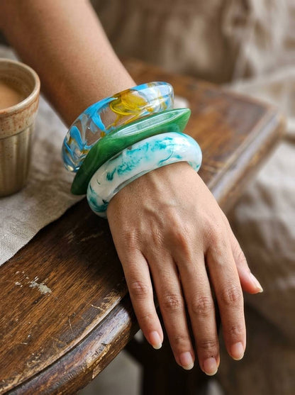Three resin marble bangles stacked on a woman's wrist resting on a wooden chair arm