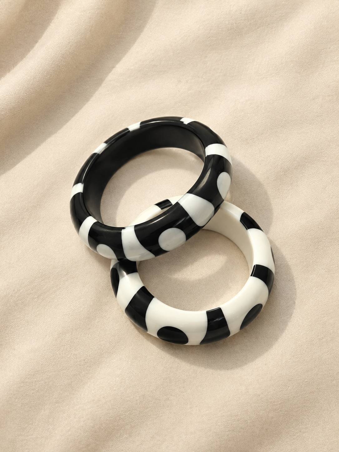 Black-base and white-base resin bangles with contrasting dot and stripe pattern placed side by side on a soft cream fabric surface