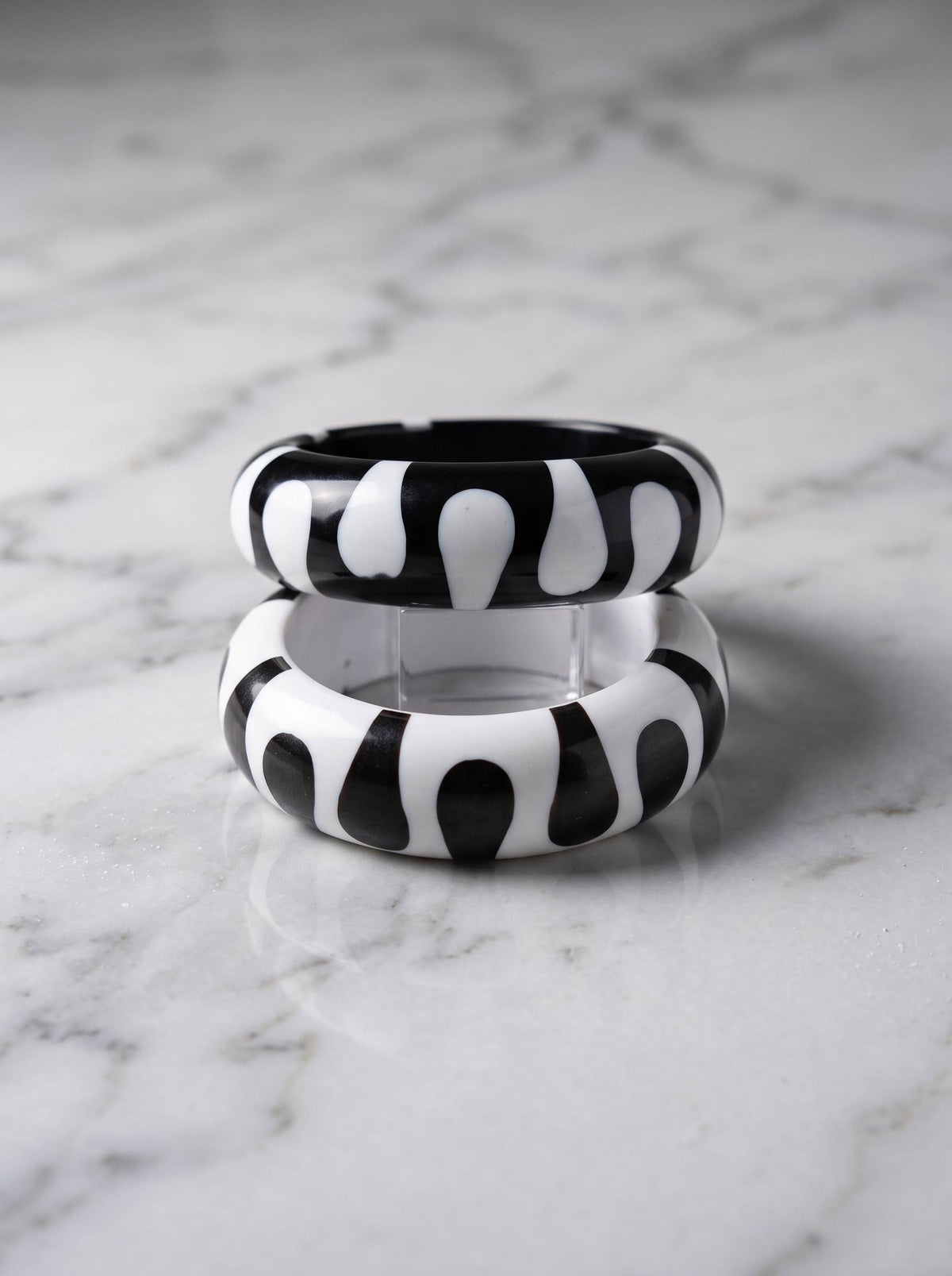 Two resin bangles with bold black and white graphic pattern stacked vertically on a white marble surface showing their rounded profile