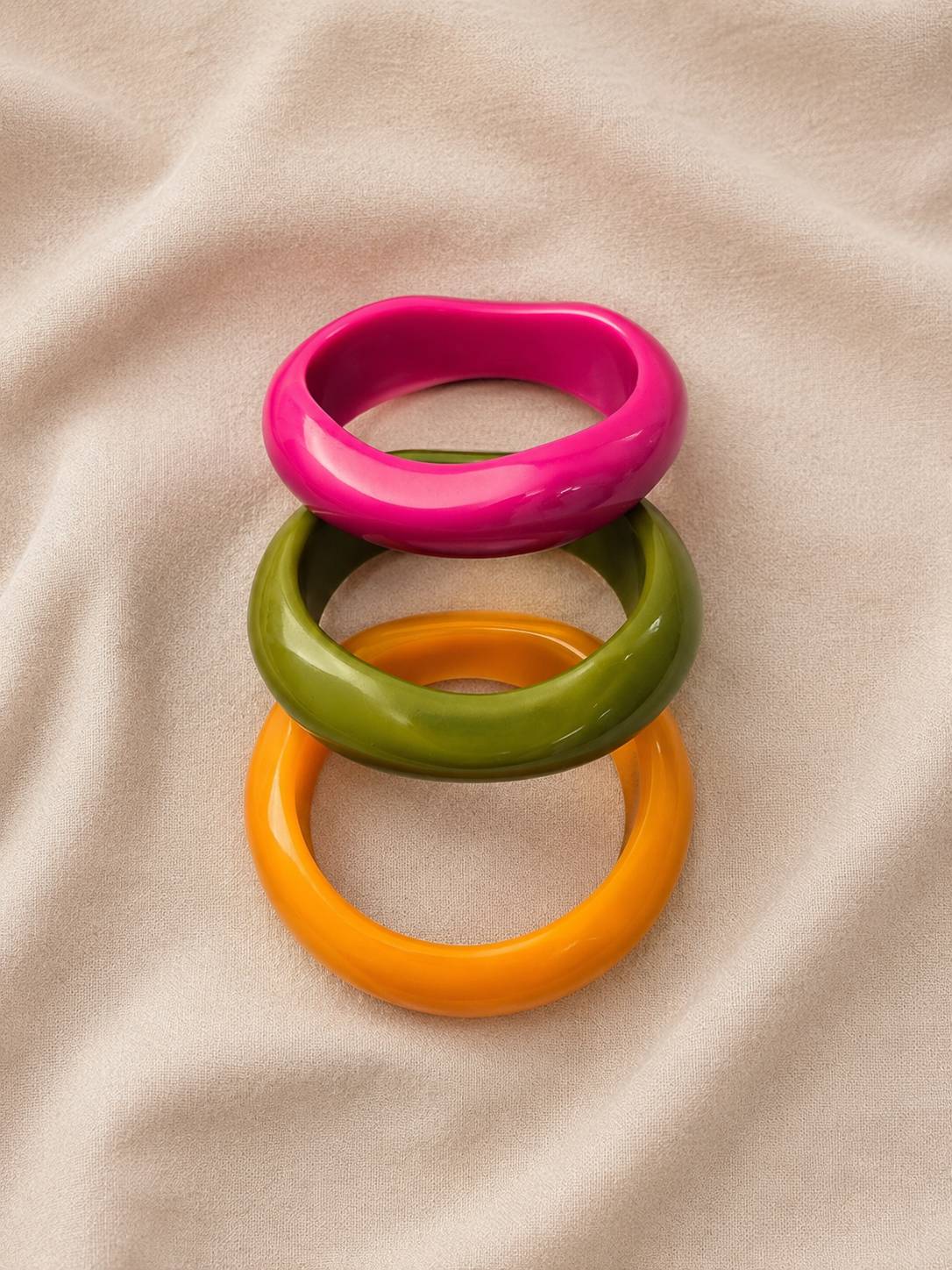 Set of three colourful resin bangles laid flat and slightly fanned on a soft linen background