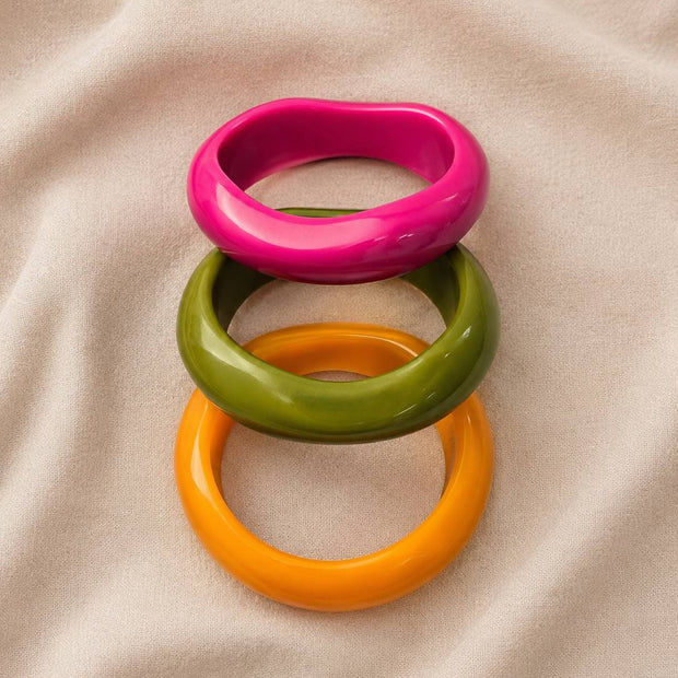 Set of three colourful resin bangles laid flat and slightly fanned on a soft linen background