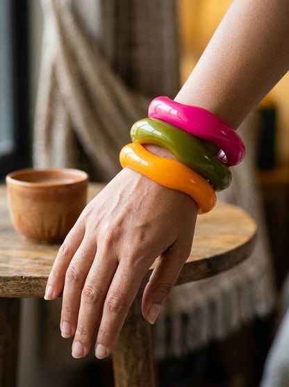 Woman wearing three stacked glossy resin bangles on her wrist resting on a wooden stool