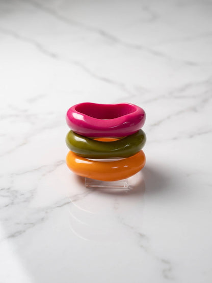 Pink, olive and orange resin bangles stacked on a clear acrylic stand against a white marble surface