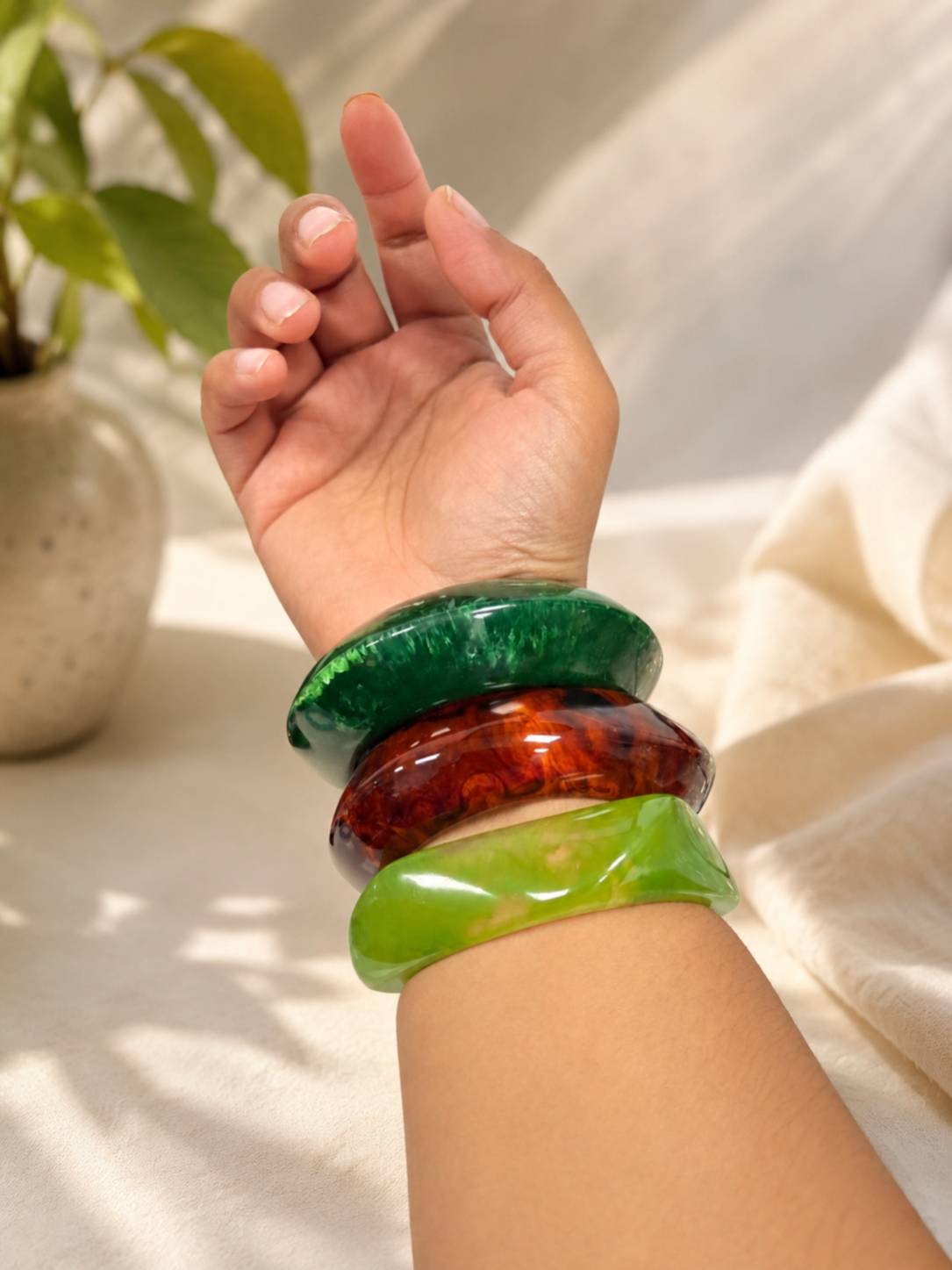 Three resin bangles stacked on a woman's wrist showing green, tortoiseshell, and lime green bangles