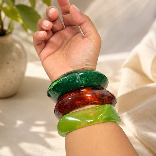 Three resin bangles stacked on a woman's wrist showing green, tortoiseshell, and lime green bangles