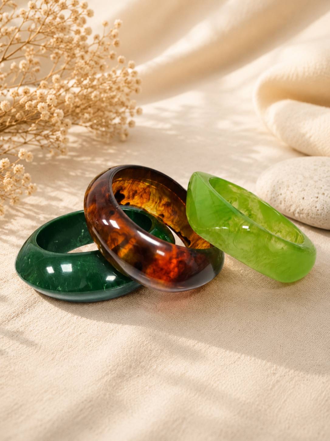 Three individual resin bangles laid flat — dark green, tortoiseshell amber, and translucent lime green