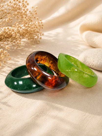 Three individual resin bangles laid flat — dark green, tortoiseshell amber, and translucent lime green