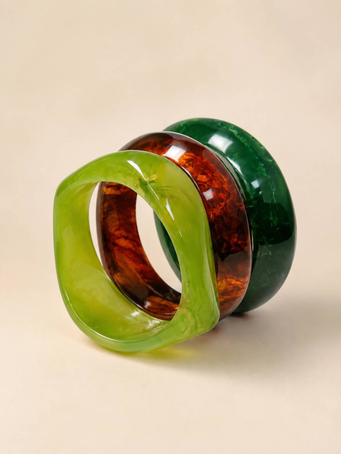 Lime green twisted resin bangle leaning against tortoiseshell and forest green bangles on a beige background