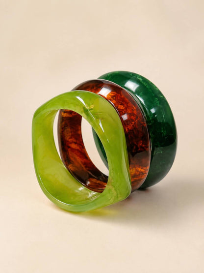 Lime green twisted resin bangle leaning against tortoiseshell and forest green bangles on a beige background