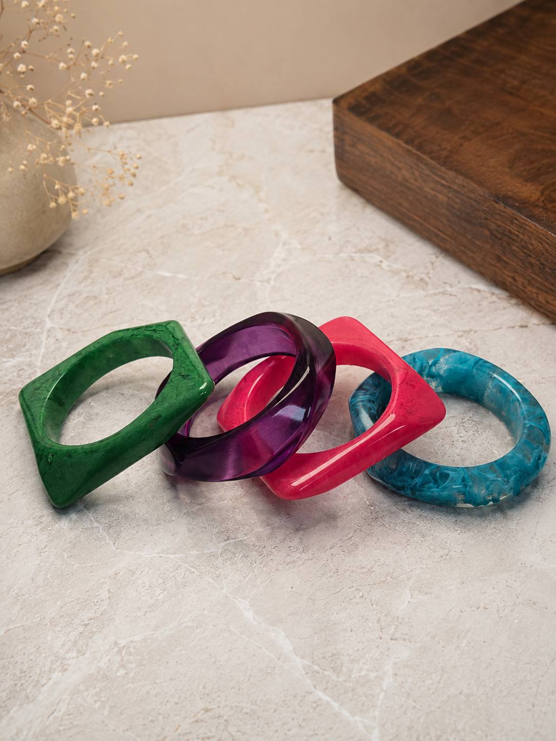 Four colourful resin marble bangles laid flat on a marble surface — green, purple, pink, and teal