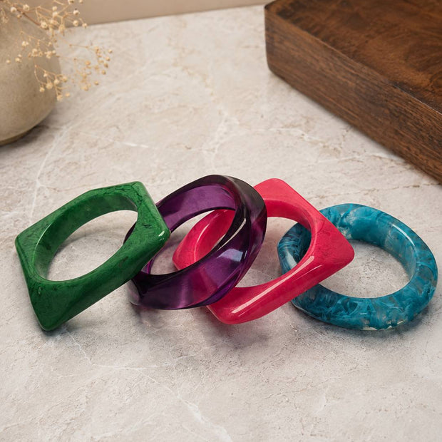 Four colourful resin marble bangles laid flat on a marble surface — green, purple, pink, and teal
