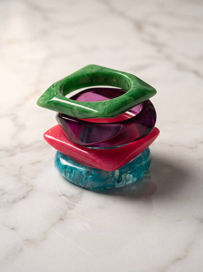 Set of four resin bangles stacked vertically on white marble showing geometric and round silhouettes