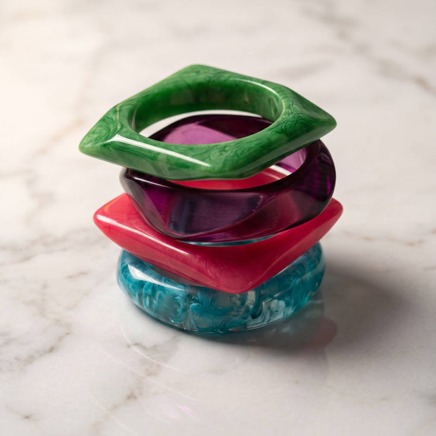 Set of four resin bangles stacked vertically on white marble showing geometric and round silhouettes