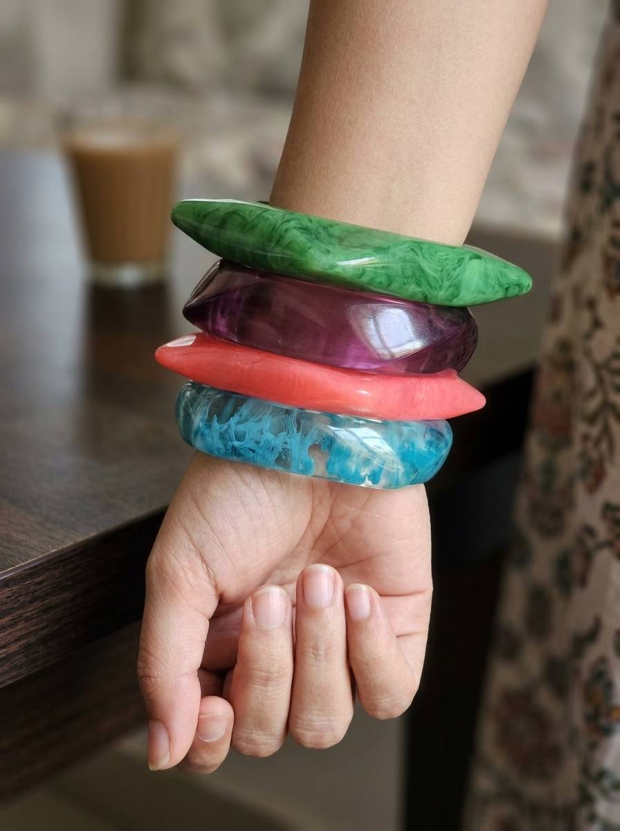 All four resin marble bangles worn stacked on a woman's wrist resting on a wooden table