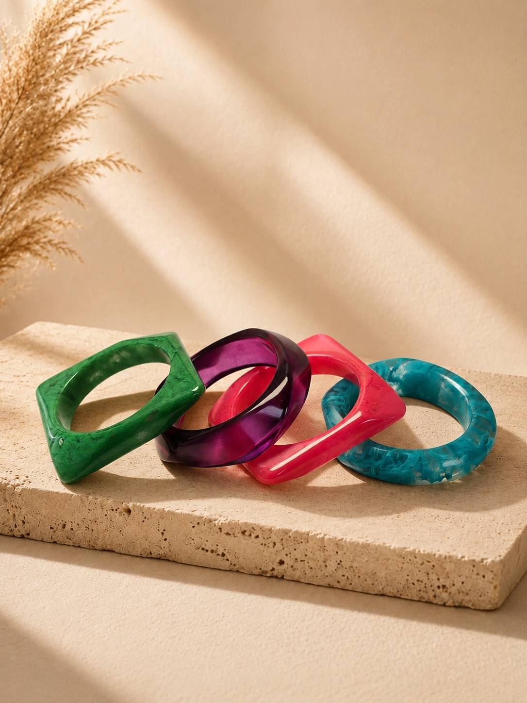 Four resin marble bangles fanned out on a textured stone surface with dried pampas grass in background