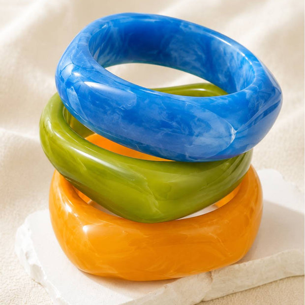 Three glossy resin marble bangles in blue, green, and orange stacked on a white stone block
