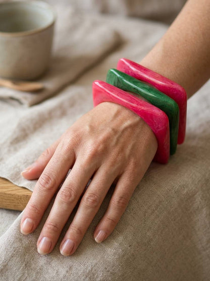 Three stacked square marble resin bangles worn on a woman's wrist resting on linen cloth