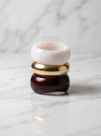 Three dome bangles stacked vertically on an acrylic stand showing burgundy, gold and pale pink resin finishes on marble surface