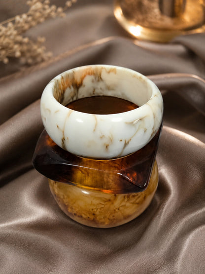 Ivory marble resin bangle stacked with tortoiseshell and amber bangles displayed on a draped satin fabric