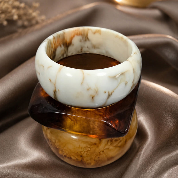 Ivory marble resin bangle stacked with tortoiseshell and amber bangles displayed on a draped satin fabric