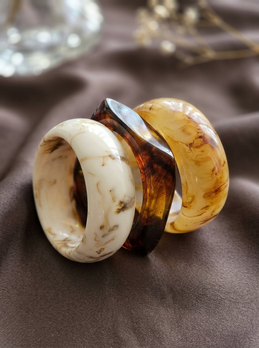 Ivory white and amber resin marble bangles leaning together on grey satin with dried florals in background