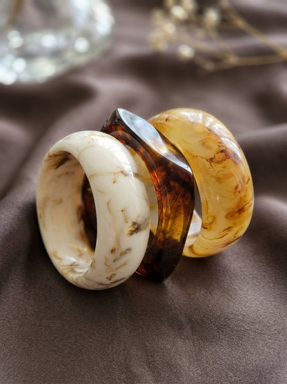 Ivory white and amber resin marble bangles leaning together on grey satin with dried florals in background