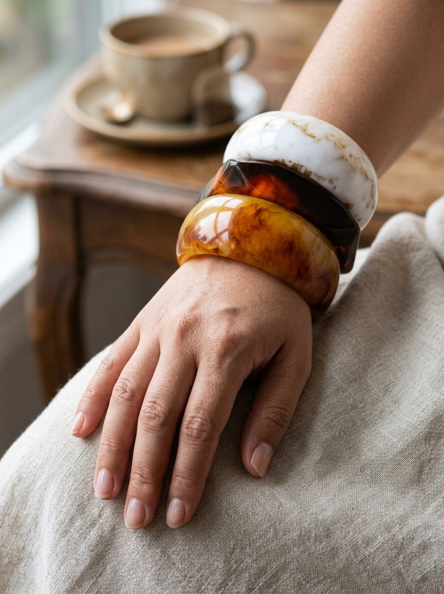 All three resin marble bangles stacked on a woman's wrist resting on a linen fabric with coffee cup behind