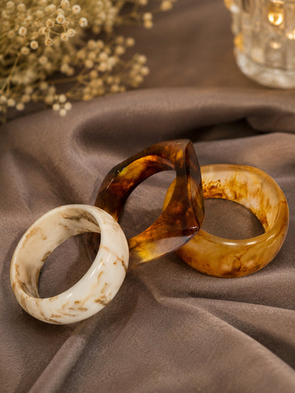 Three resin marble bangles in ivory, tortoiseshell, and amber arranged on grey satin with baby's breath flowers