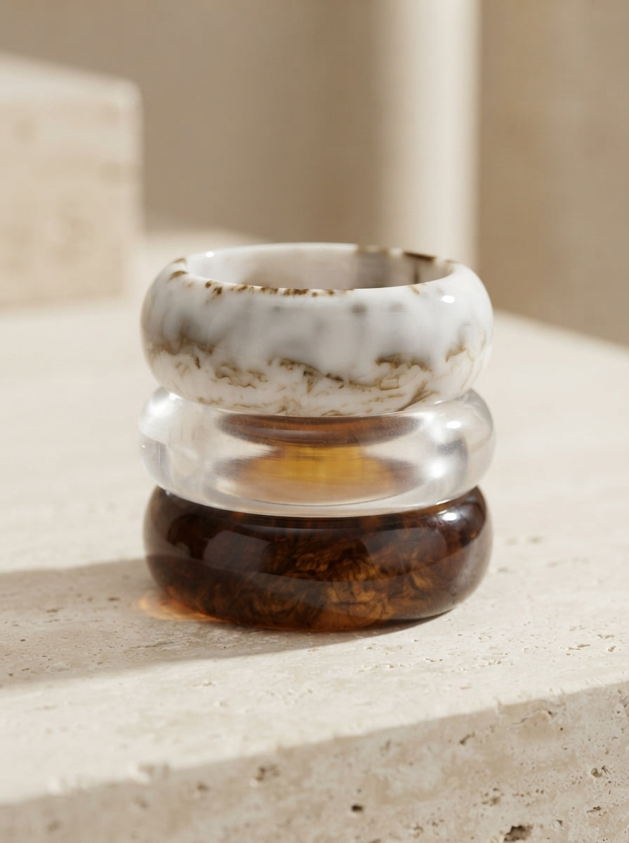 Stack of three resin bangles piled on travertine stone showing marble, clear, and tortoise finishes from above