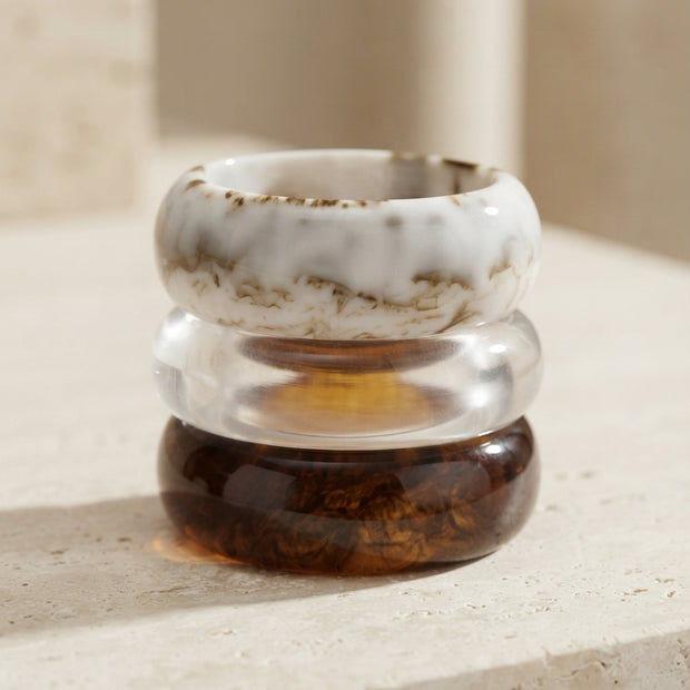 Stack of three resin bangles piled on travertine stone showing marble, clear, and tortoise finishes from above