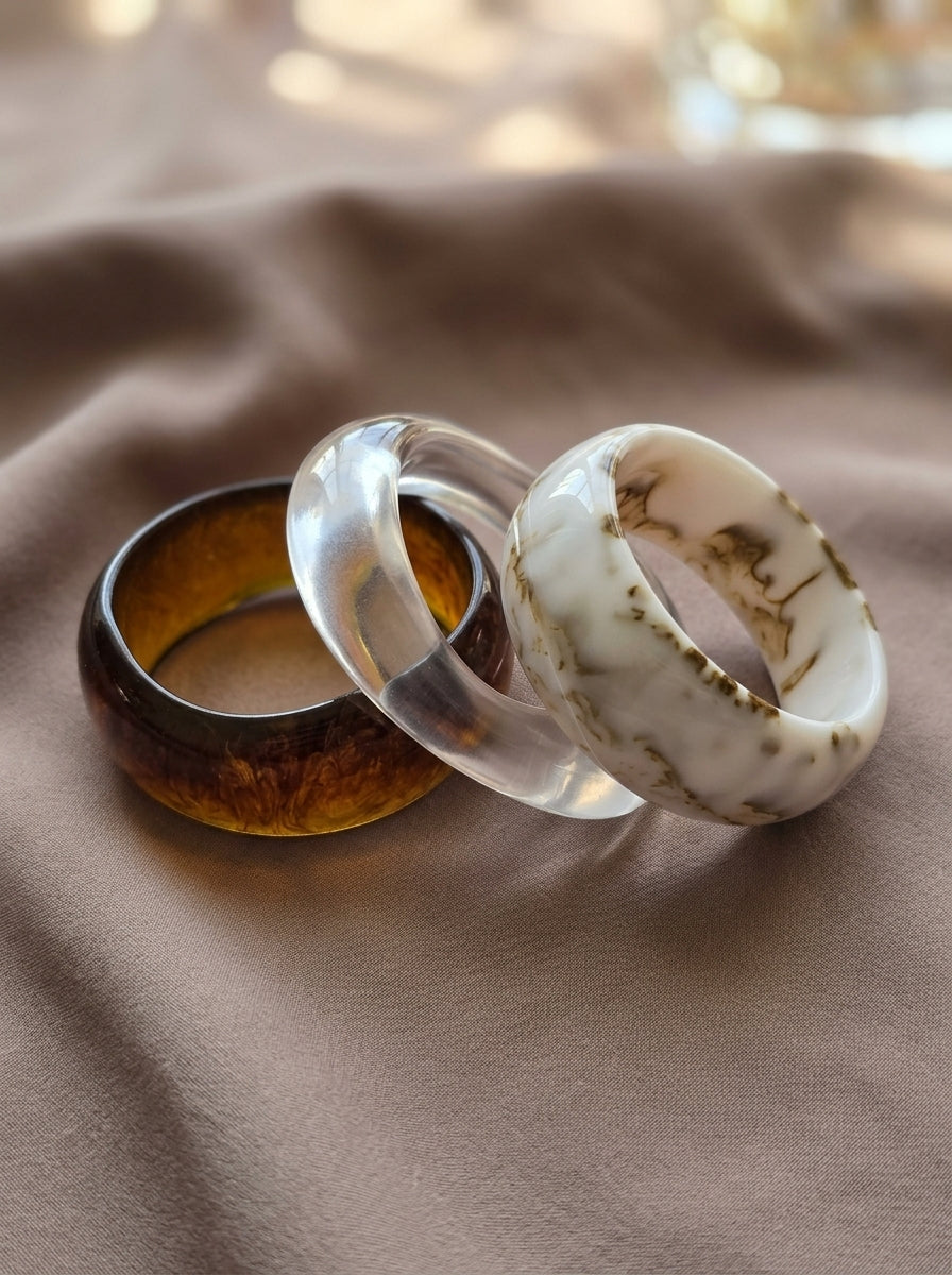 Amber tortoise, clear crystal, and white marble resin bangles arranged overlapping on beige fabric