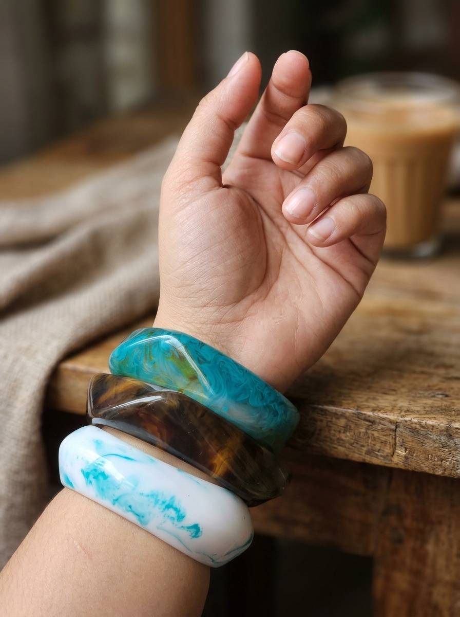 Three resin marble bangles stacked on a woman's wrist raised against a wooden table background
