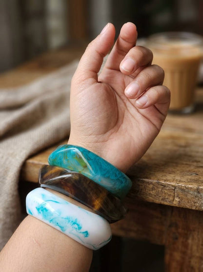 Three resin marble bangles stacked on a woman's wrist raised against a wooden table background