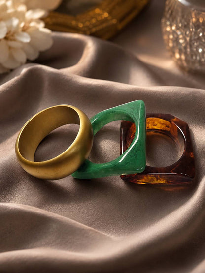Three stacked bangles laid flat on satin — gold-tone, green marbled resin, and amber tortoiseshell resin