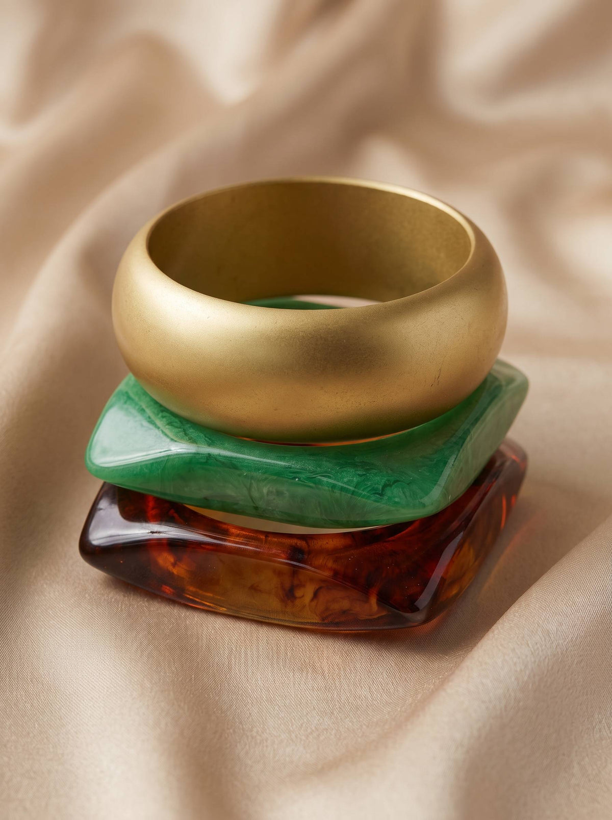 Side view of three bangles stacked vertically — gold-tone on top, green resin in middle, tortoiseshell resin at base