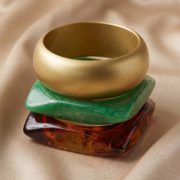 Side view of three bangles stacked vertically — gold-tone on top, green resin in middle, tortoiseshell resin at base