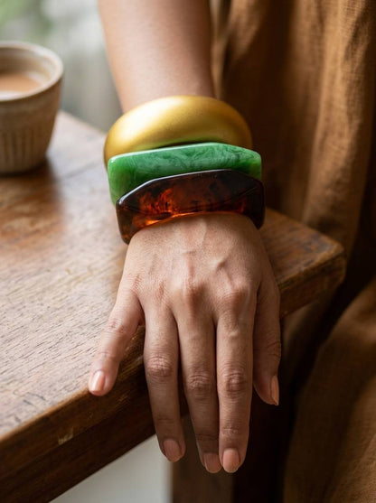 Woman wearing all three stacked bangles on her wrist resting on a wooden table edge