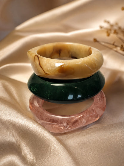 Amber, green, and rose marble resin bangles stacked on golden satin fabric with dried flowers