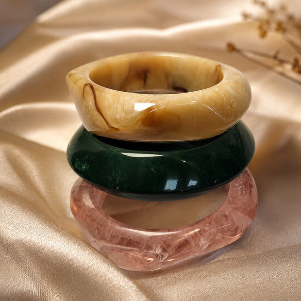 Amber, green, and rose marble resin bangles stacked on golden satin fabric with dried flowers