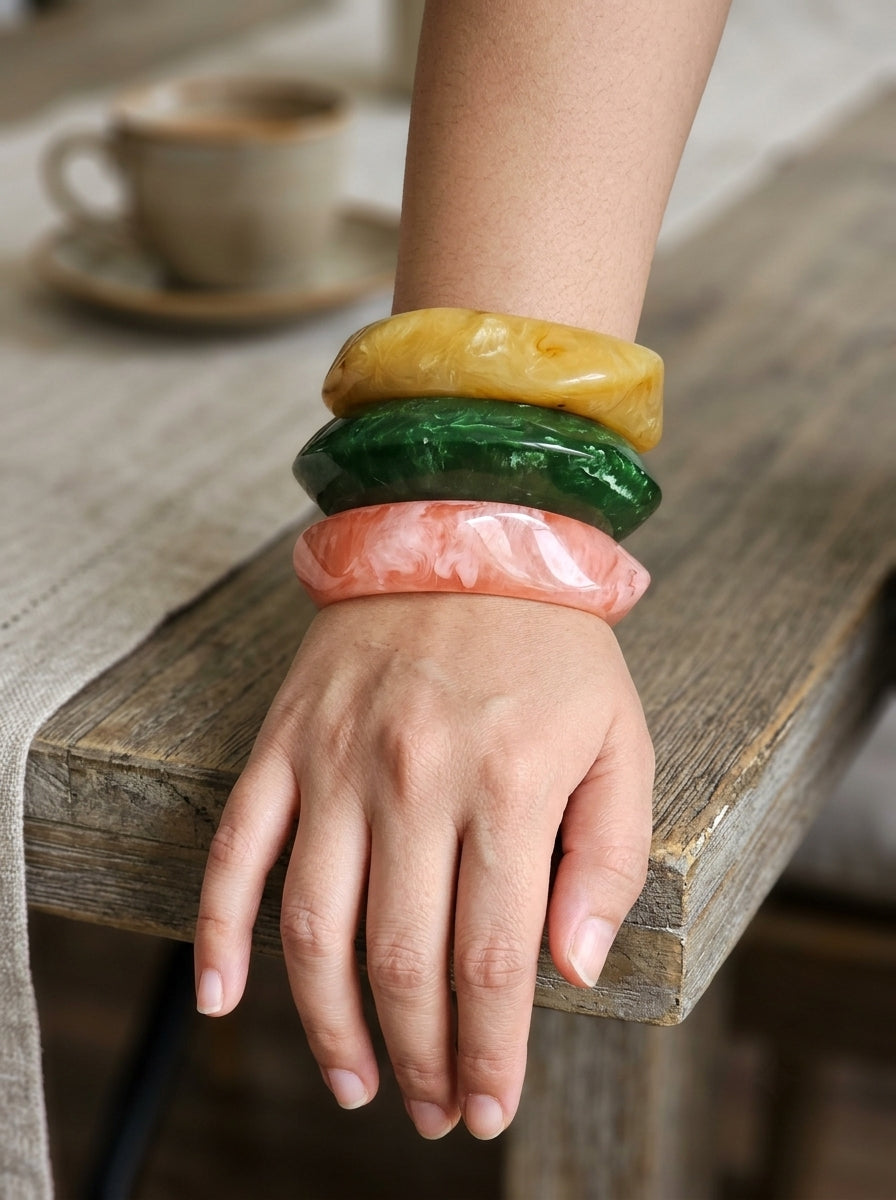 All three marble resin bangles worn stacked on a woman's wrist resting on a wooden table