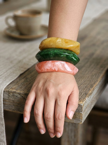 All three marble resin bangles worn stacked on a woman's wrist resting on a wooden table